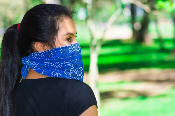 Mujer morena joven con bandana azul cubriendo la mitad de la cara, interactuando al aire libre para la cámara, concepto de protesta activista — Foto de Stock