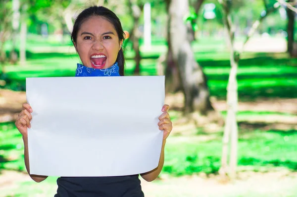 Giovane donna bruna indossa bandana blu intorno al collo, tenendo poster bianco cantando all'aperto di fronte alla telecamera, concetto di protesta attivista — Foto Stock
