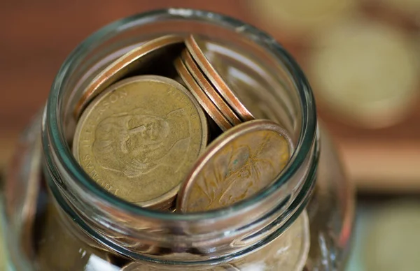 Close up glass jar opening filled up with dollar coins — Stock Photo, Image