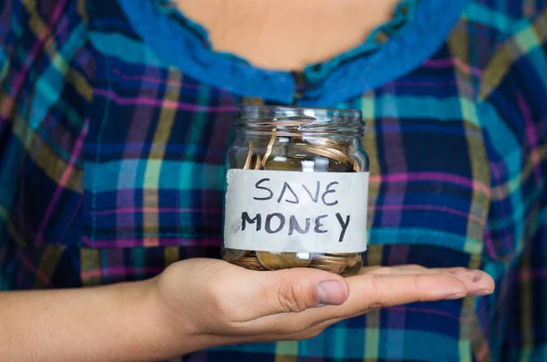Donna di fronte alla macchina fotografica, tenendo in mano vaso di vetro con monete all'interno, lettura etichetta risparmiare denaro — Foto Stock