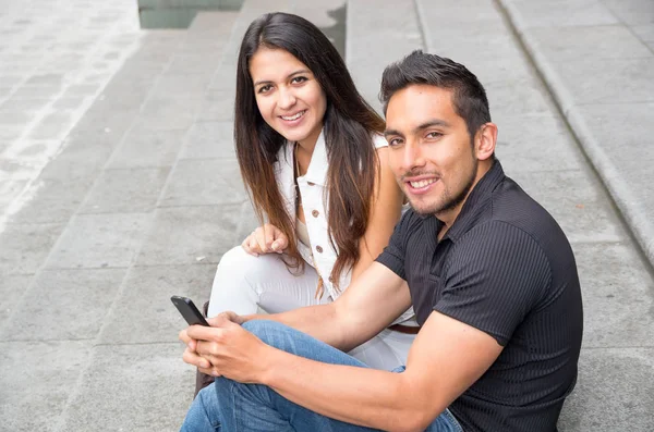 Encantador jovem casal sentado em etapas de construção usando telefone celular e interagindo feliz, conceito turístico urbano — Fotografia de Stock