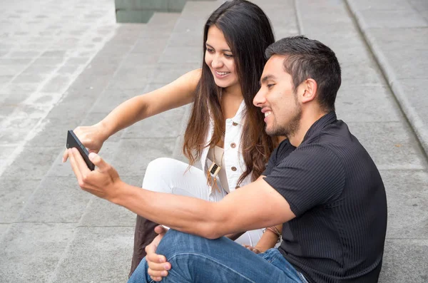 Encantadora pareja joven sentada en la construcción de escalones utilizando el teléfono móvil e interactuando felizmente, concepto turístico urbano — Foto de Stock