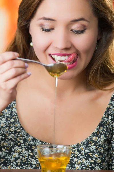 Mujer joven frente a la cámara sosteniendo cuchara con miel goteando en un vaso pequeño en la mesa — Foto de Stock