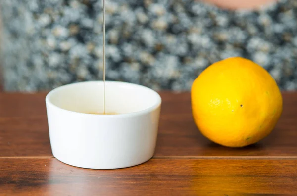 Stäng upp liten vit kopp sitter på trä skrivbord med honung som faller in i den ovanifrån, citron på sida — Stockfoto