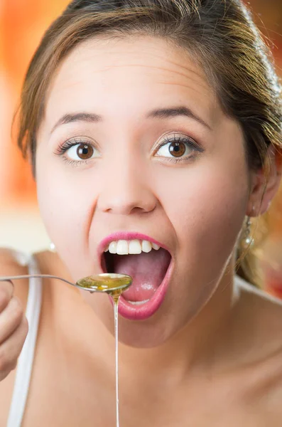 Young woman facing camera holding spoon with honey dripping over edge, mouth open as ready to eat — Stock Photo, Image