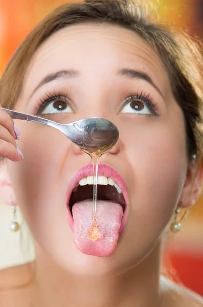 Mujer joven frente a la cámara sosteniendo la cuchara con miel goteando en su lengua —  Fotos de Stock