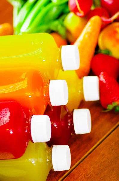 Botellas de delicioso jugo orgánico en el escritorio rodeado de frutas y verduras, hermosos colores, concepto de estilo de vida saludable —  Fotos de Stock