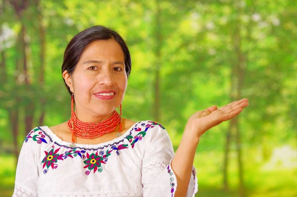 Closeup mooie Spaanse vrouw het dragen van traditionele Andes witte blouse met kleurrijke decoratie om nek, bijpassende rode ketting en oor, gelukkig poseren voor de camera stak handpalm, Tuin — Stockfoto