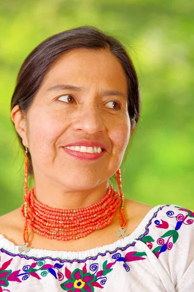 Närbild vackra spansktalande kvinna som bär traditionella andinska vit blus med färgglada dekoration runt hals, matchande röda halsband och öra, poserar glatt för kamera, trädgård bakgrund — Stockfoto