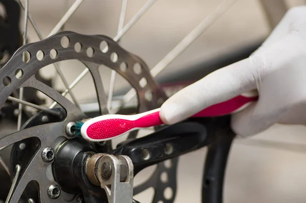 Closeup hand dragen witte handschoen holding tandenborstel wrijven op metalen fietsketting, mechanische reparatie concept — Stockfoto