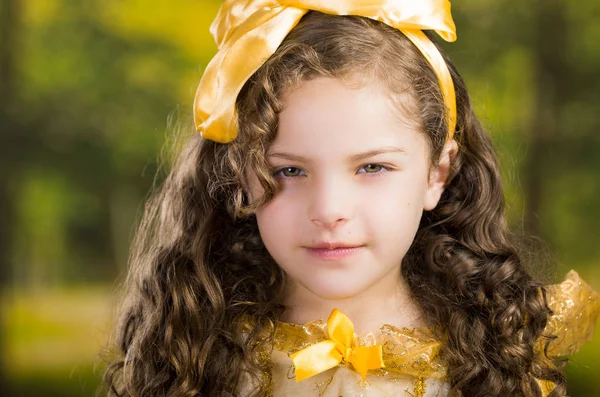 Headshot schattig klein meisje dragen mooie gele jurk met bijpassende hoofdband, poseren voor de camera, groene bos achtergrond — Stockfoto