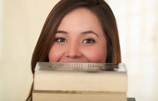 Junge hübsche Frau versteckt sich lächelnd hinter aufgeschlagenem Buch — Stockfoto