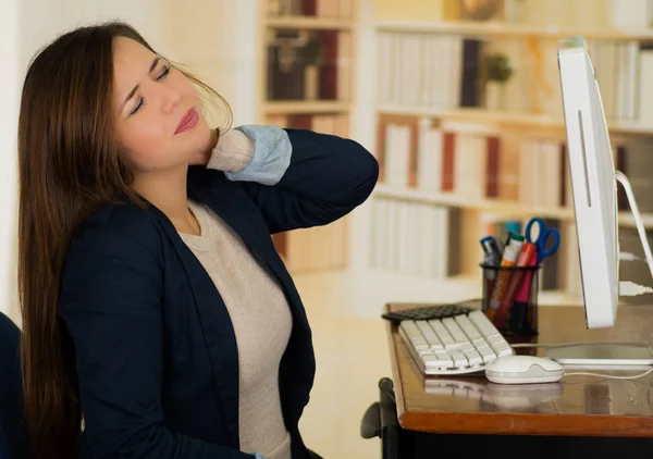 Femme d'affaires fatiguée ayant un mal de cou tout en travaillant sur son ordinateur portable dans un bureau lumineux — Photo