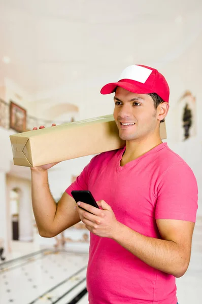 Entrega hombre en uniforme rosa sosteniendo una caja sobre sus hombros — Foto de Stock