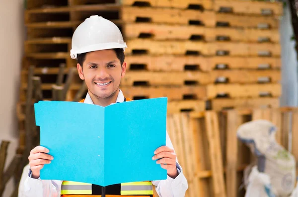 Smiling young engineer holding a folder at construction site — Stock Photo, Image