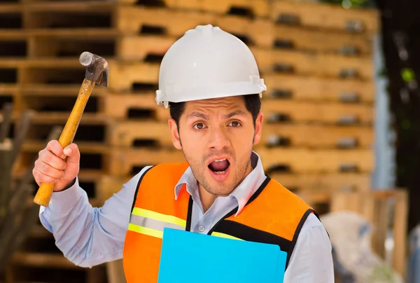 Knappe jonge ingenieur die een map en hamer in zijn hand op bouwplaats krijgen gek — Stockfoto