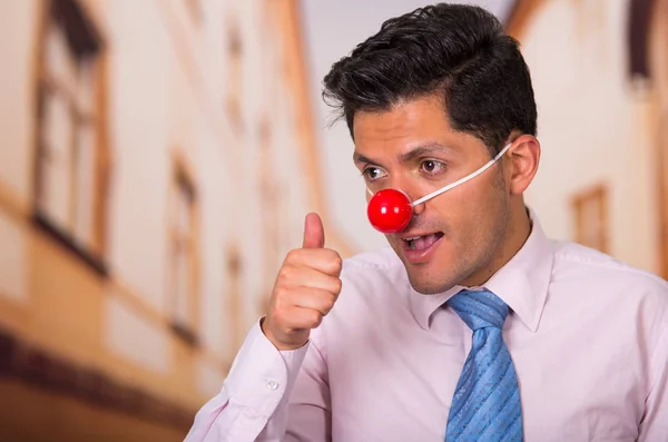Divertido hombre de negocios guapo con la nariz de plástico rojo con el pulgar hacia arriba aprobando algo . — Foto de Stock
