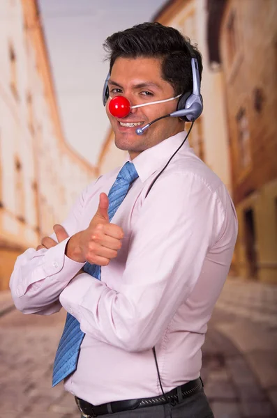 Divertido hombre de negocios guapo con la nariz de plástico rojo usando auriculares y se ve sorprendido . —  Fotos de Stock