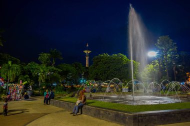Banyuwangi, Endonezya: yeşil bitki örtüsü ve popüler su çeşme, zevk insanlar, güzel mavi akşam gökyüzü arka planda ile park alanı büyüleyici