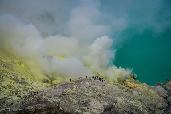KAWEH IJEN, INDONESIA: Tourist hikers with backpacks and facial masks seen overlooking sulfur mine and volcanic crater — Stock Photo, Image