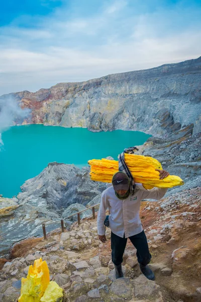 Με ωραία... Kaweh, Ινδονησία - 3 Μαρτίου 2017: τοπικές ανθρακωρύχους που μεταφέρουν βαριά φορτία των βράχων κίτρινο θείου επάνω στην πλευρά του βουνού, πεζοπορία έλξης τουριστών βρίσκεται στο εσωτερικό ηφαιστειακό κρατήρα, θεαματική φύση — Φωτογραφία Αρχείου