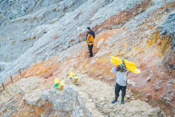 KAWEH IJEN, INDONESIA - 3 MARCH, 2017: Local miners carrying heavy loads of yellow sulfur rocks up mountain side, tourist hiking attraction located inside volcanic crater, spectacular nature
