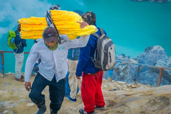 Kaweh ijen, indonesien - 3. März 2017: Bergleute tragen schwere Ladungen gelben Schwefelgesteins den Berg hinauf, Touristenattraktion im Inneren des Vulkankraters, spektakuläre Natur — Stockfoto