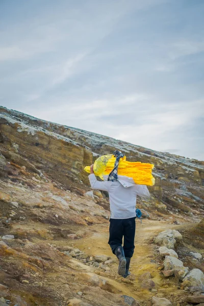 Kaweh ijen, indonesien: lokaler Bergmann trägt schwere Ladung gelber Schwefelgesteine die Berghänge hinauf, touristische Wanderattraktion im Inneren des Vulkankraters, spektakuläre Natur — Stockfoto