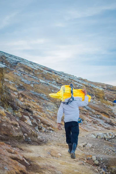 Kaweh ijen, indonesien: lokaler Bergmann trägt schwere Ladung gelber Schwefelgesteine die Berghänge hinauf, touristische Wanderattraktion im Inneren des Vulkankraters, spektakuläre Natur — Stockfoto