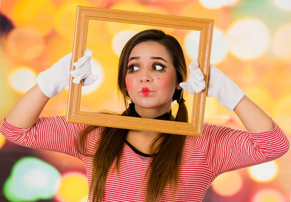 Closeup portrait of cute curious young girl clown mime holding wooden frame looking to the side — Stock Photo, Image