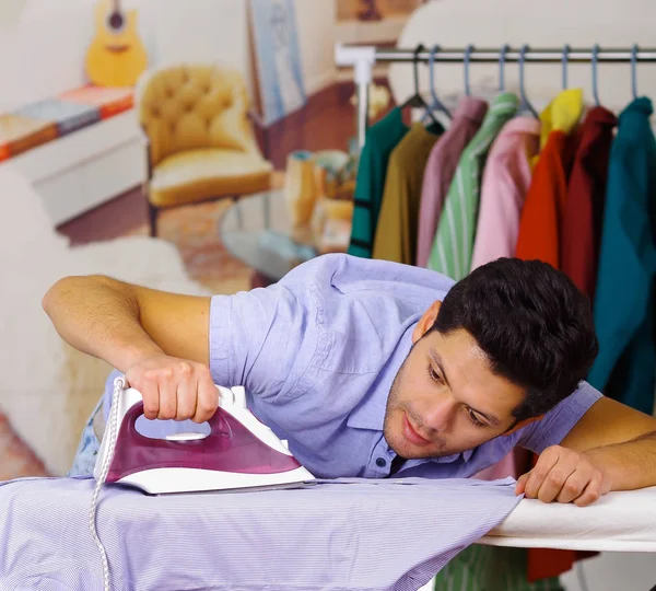 Primer plano de un joven guapo planchando ropa en la tabla de planchar — Foto de Stock
