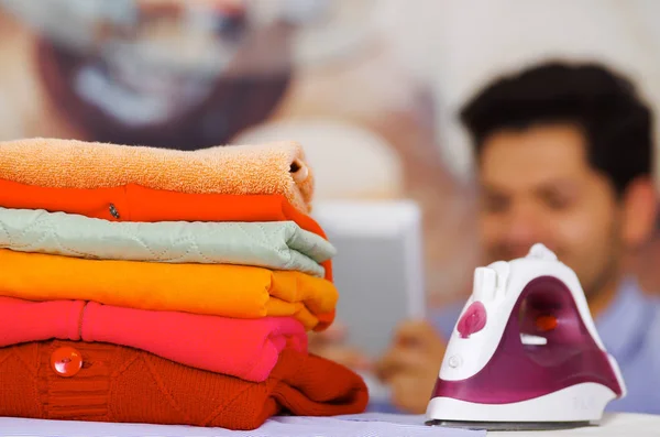 Una pila de ropa al lado de la plancha con un hombre hermoso sonriendo detrás — Foto de Stock