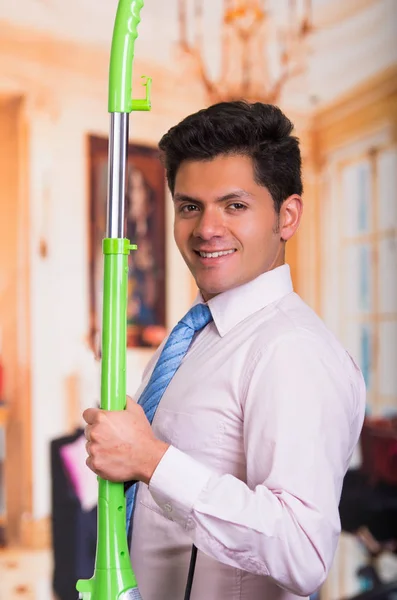 Hombre joven guapo limpiando casa con una aspiradora verde —  Fotos de Stock