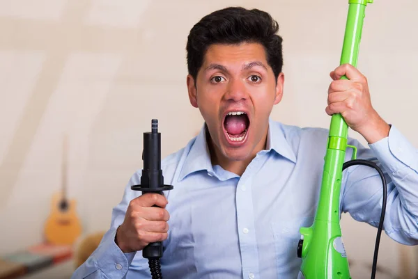 Handsome young Man holding a vacuum cleaner and screaming — Stock Photo, Image