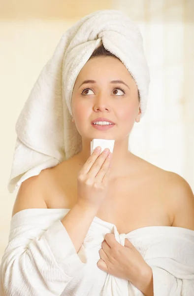 Bezorgd mooie jonge vrouw met een witte handdoek die betrekking hebben op haar hoofd is het reinigen van haar kin met een klein stukje papier in de badkamer — Stockfoto