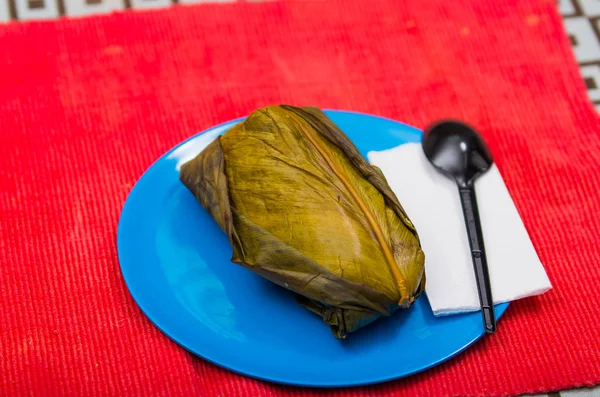 Un delizioso Tamal viene servito su un piatto blu che è sopra una tovaglia rossa, con un cucchiaio e un tovagliolo. Concetto di cibo tradizionale andino — Foto Stock