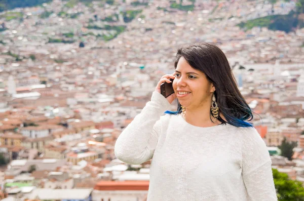 Latin kislány, segítségével a mobiltelefon, a háta mögött egy gyönyörű gyarmati város — Stock Fotó