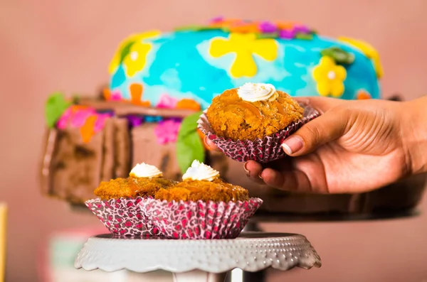 Mano che tiene un muffin delizioso di colore marrone, grande torta colorata sullo sfondo, concetto di pasticceria — Foto Stock