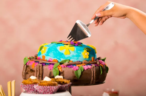 Taglio a mano in deliziosa torta colorata utilizzando strumento da cucina in metallo, sfondo rosa carta da parati, concetto di pasticceria — Foto Stock