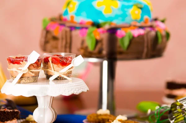 Köstliche Mousse bedeckt mit Erdbeerbelag, präsentiert in kleinen Gläsern mit angehängten Löffeln, buntem Tortenhintergrund, Gebäckkonzept — Stockfoto