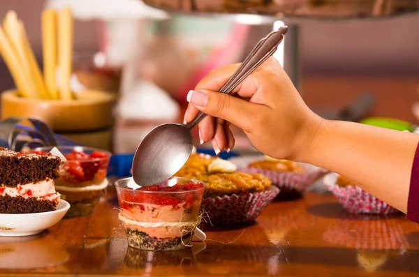 Deliziosa mousse ricoperta di guarnizione alla fragola, presentata all'interno di piccoli bicchieri, morso afferrando cucchiaio mano, pezzi di torta e sfondo muffin, concetto di pasticceria — Foto Stock