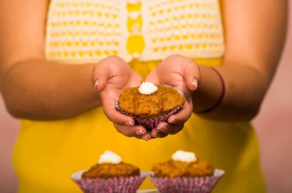 Donna che tiene delizioso muffin marrone colorato con crema topping, mostrando alla macchina fotografica, concetto di pasticceria — Foto Stock