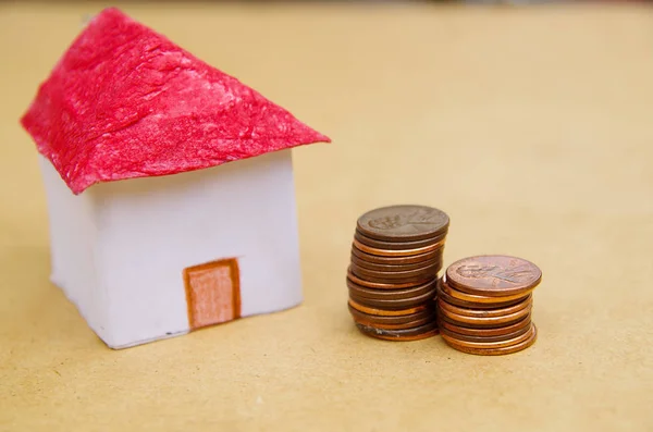 Small beautiful house with coins stacked in front of the housing model pretending: house prices, house buying, real estate, mortgage concept