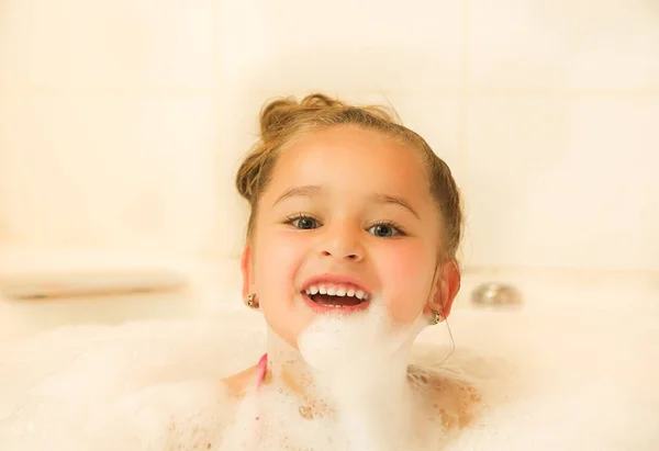 Little beautiful girl posing inside of a bathtub with water and foam in bath — Stock Photo, Image