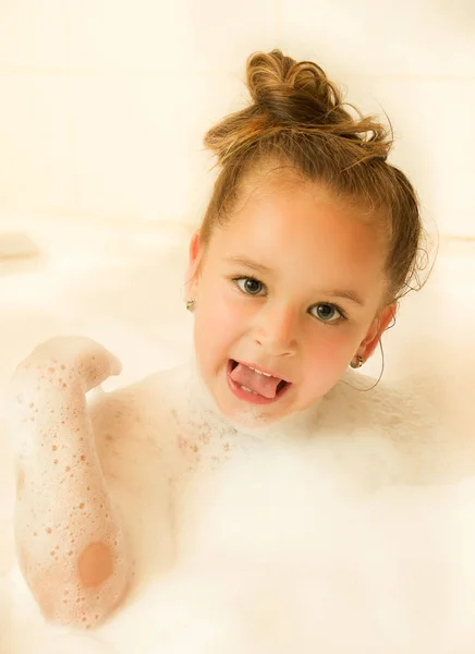 Маленькая красивая девочка позирует внутри ванны с водой и пеной в ванне Высунув язык — стоковое фото