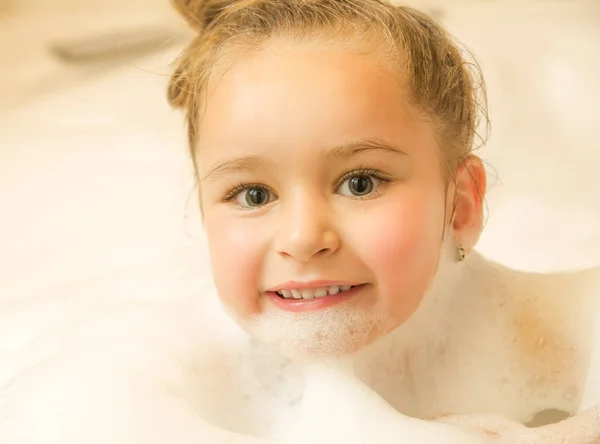 Closeup of a little beautiful girl posing inside of a bathtub with water and foam in bath — Stock Photo, Image