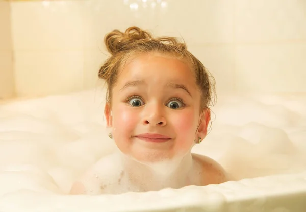 Mooi meisje poseren binnenkant van een bad met water en schuim in Bad doen van grappige gezichten — Stockfoto