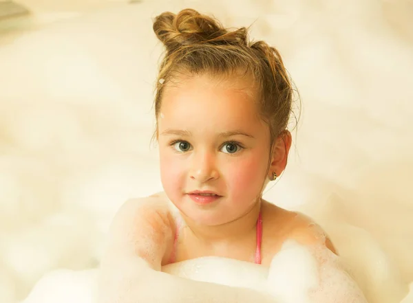 Piccola bella ragazza posa all'interno di una vasca da bagno con acqua e schiuma in bagno — Foto Stock