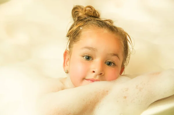 Little beautiful girl posing inside of a bathtub with water and foam in bath — Stock Photo, Image
