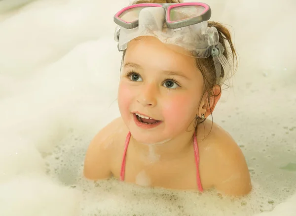 Little beautiful girl playing with water and foam in bath using a swimsuit and beautiful dive sunglasses — Stock Photo, Image